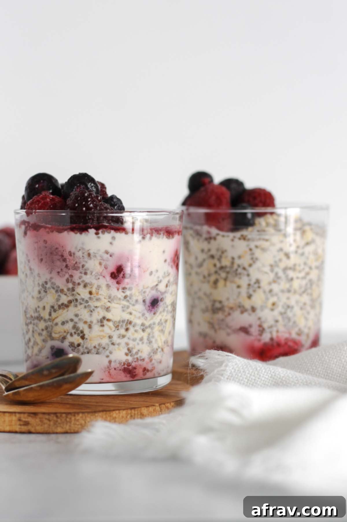 Two short glasses filled with overnight oats and topped with a mixture of frozen berries.