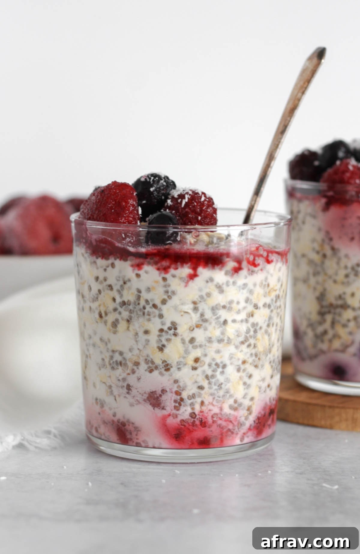 Glass cup filled with overnight oats topped with thawed frozen fruit with a vintage spoon in the glass.