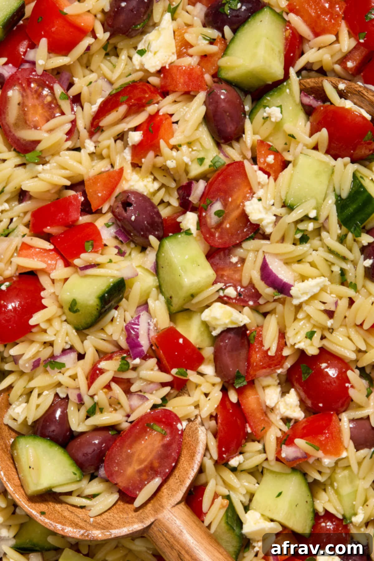 Close-up view of Greek orzo pasta salad, showing the texture of the orzo, the vibrant colors of the vegetables, and pieces of feta and olives.
