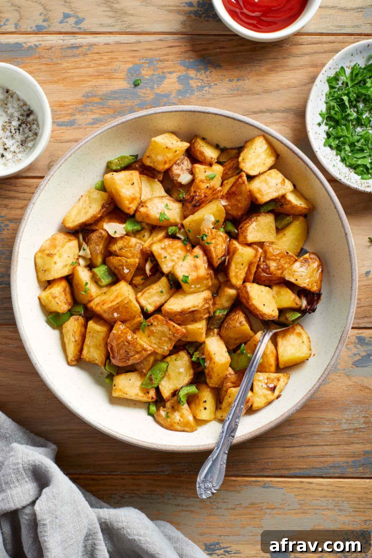Overhead view of home fries in a white bowl with a spoon inserted into it.