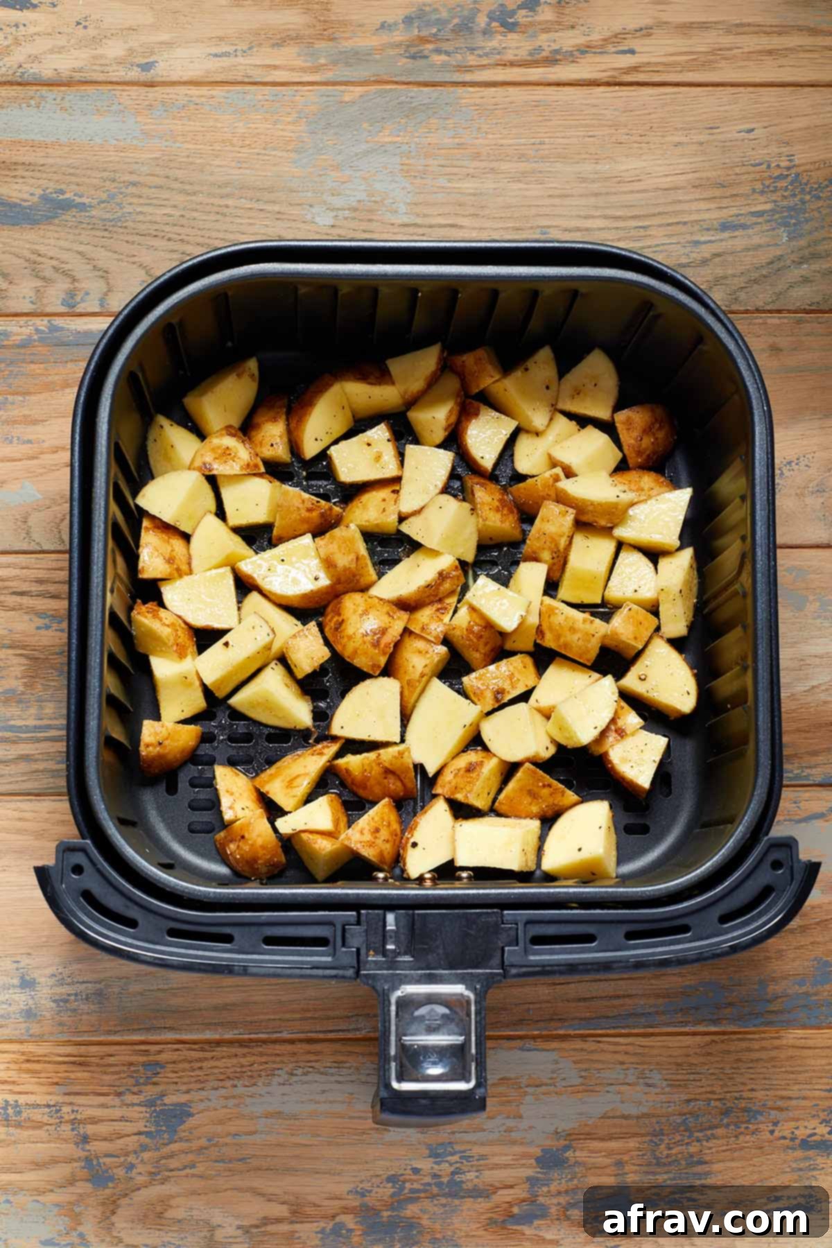 Raw, cubed and seasoned potatoes in an air fryer basket.