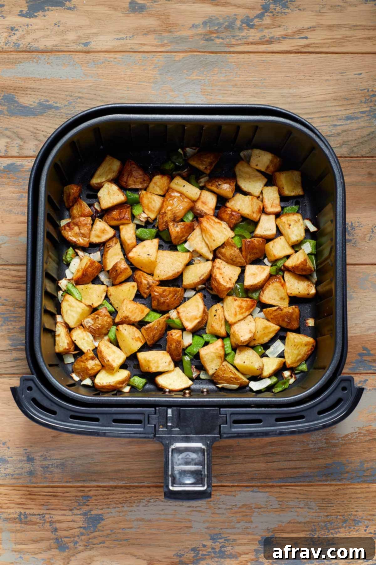Air fried potatoes, green peppers and onions in an air fryer basket.