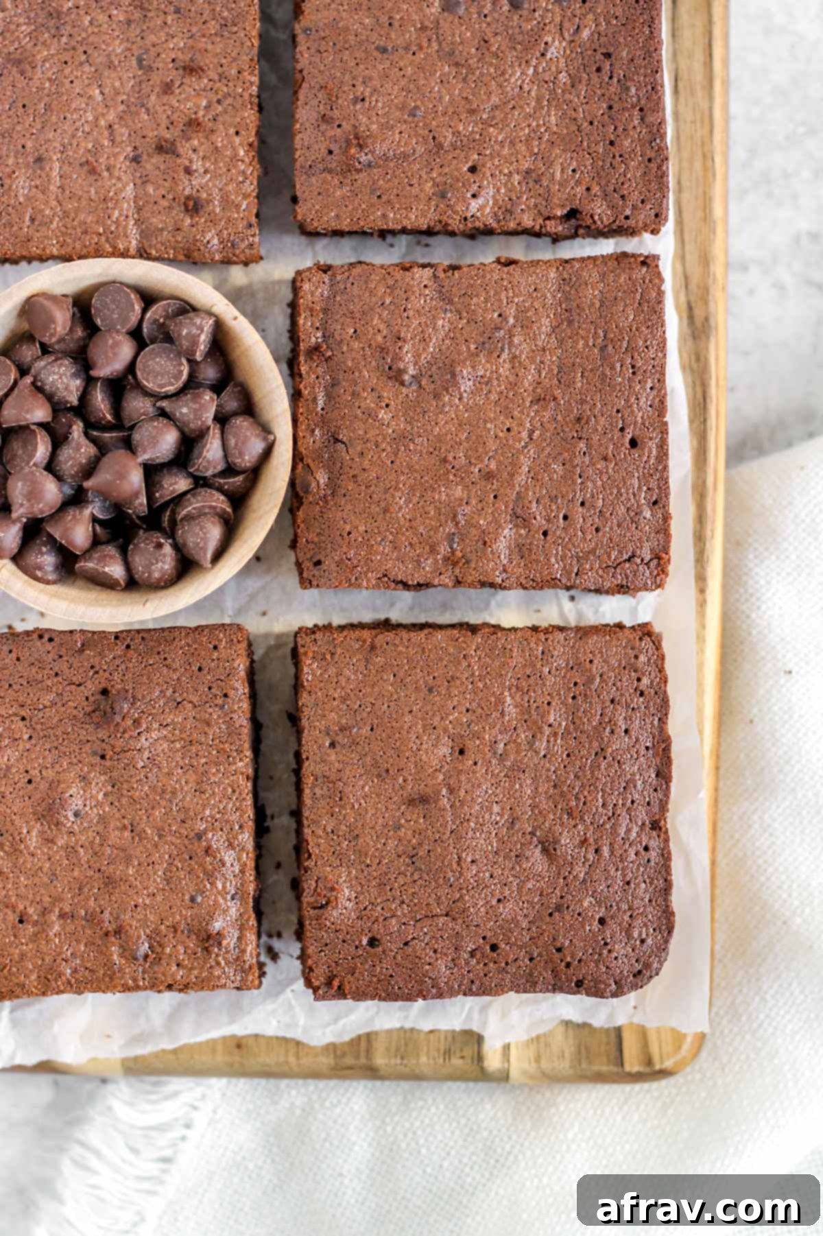 Close-up of a single fudgy oat flour brownie with chocolate chips on a wooden board.