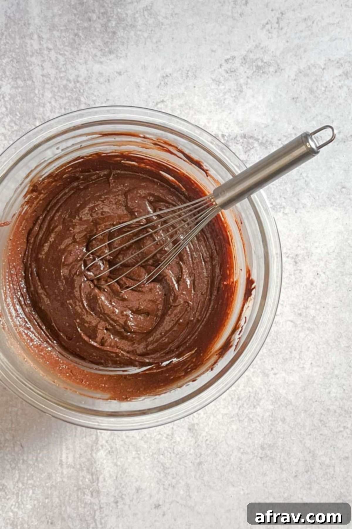 Brownie batter being whisked until smooth in a glass mixing bowl.