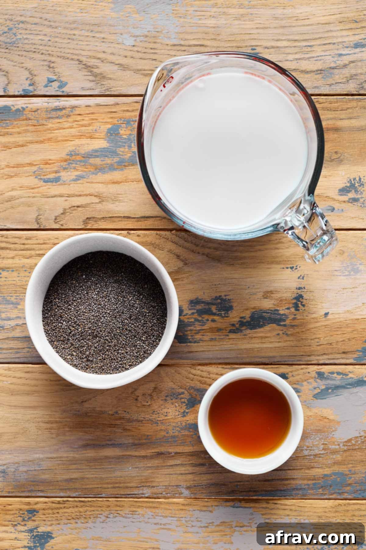 Three key ingredients for oat milk chia pudding – a bag of chia seeds, a carton of oat milk, and a bottle of maple syrup – neatly arranged on a rustic wooden table.