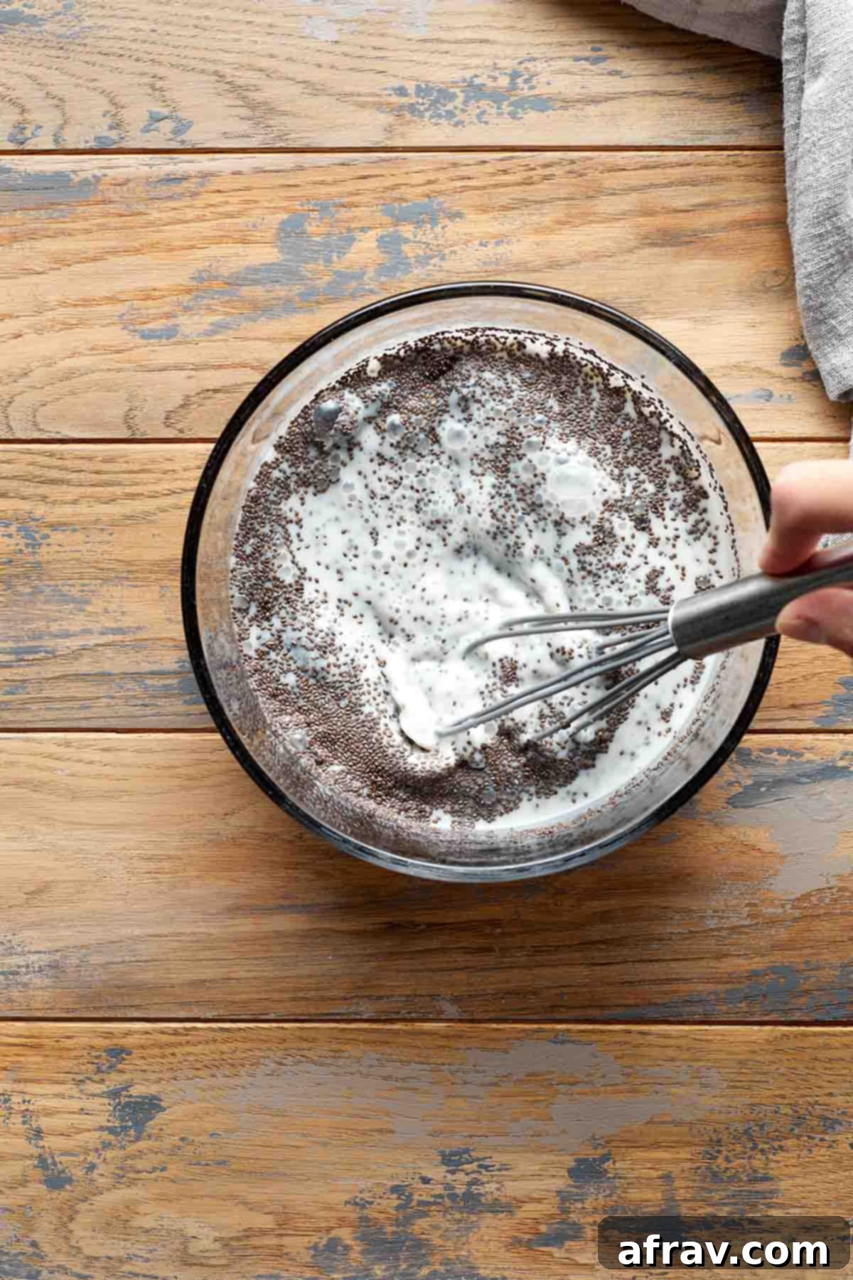 A close-up of a bowl where chia seeds, oat milk, and maple syrup are being whisked together to create the pudding base, showing the initial mixing process.