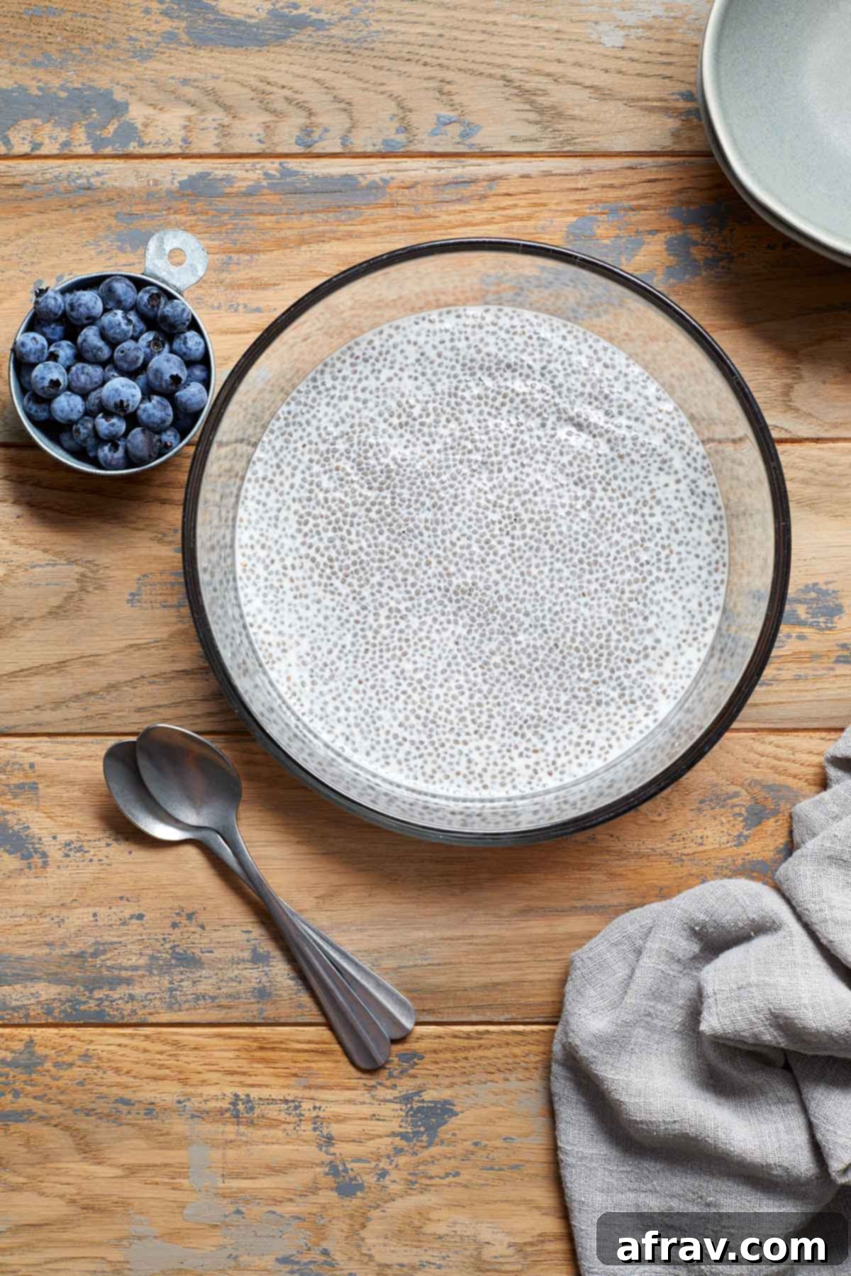 A clear glass bowl showcasing the creamy chia pudding with a handful of fresh blueberries scattered on the side, highlighting the desired texture and one potential topping.