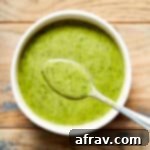 Jalapeño vinaigrette in a white bowl on a wooden table with a spoonful of vinaigrette lifted out of the bowl.
