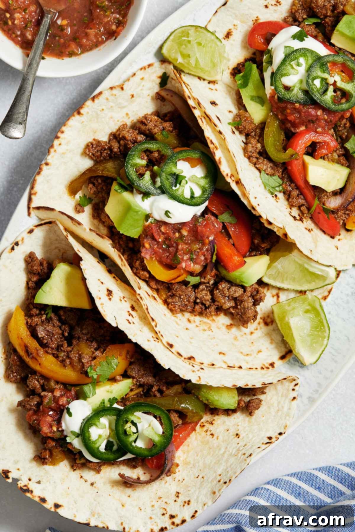 Zesty Ground Beef Fajitas 2 Close up view of ground beef fajitas on a platter and topped with sour cream, salsa and jalapeños.