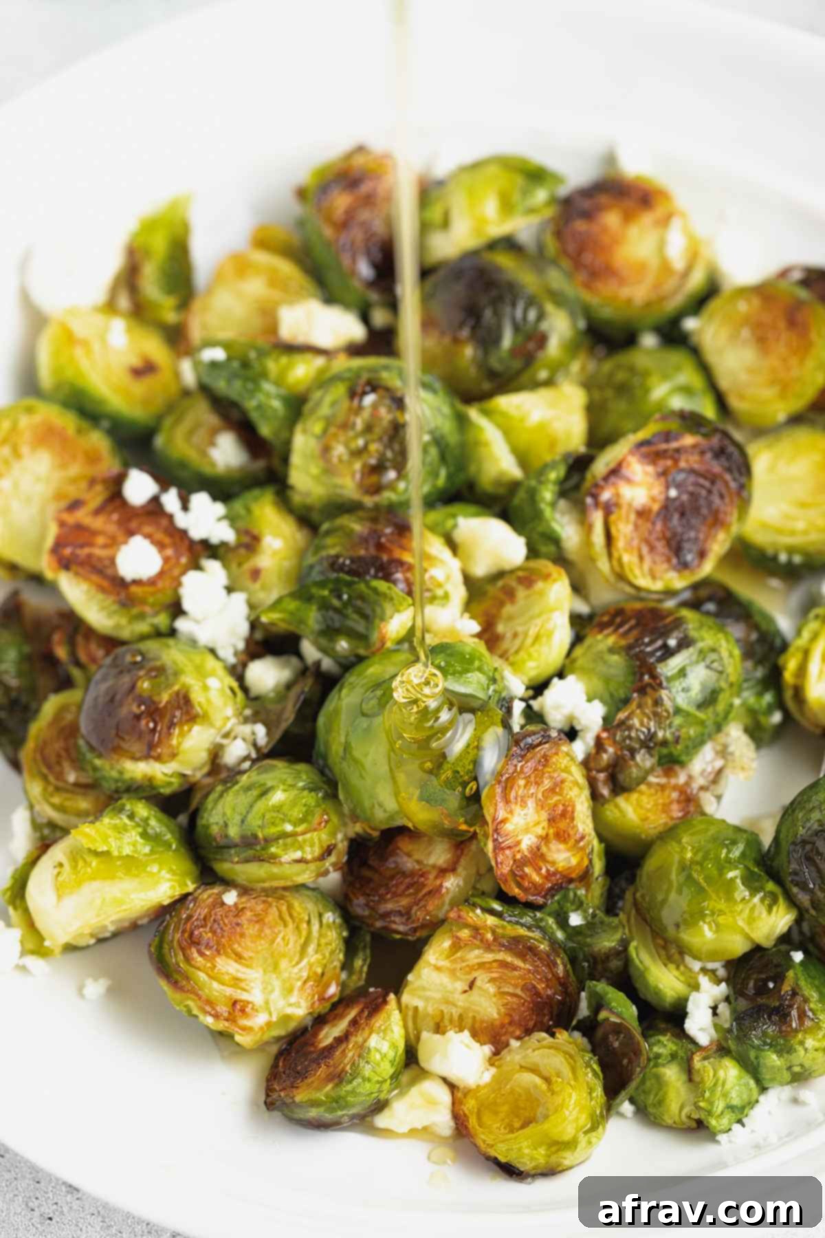 Honey being drizzled over cooked Brussels sprouts, highlighting their crispy texture and the creamy goat cheese crumbles.