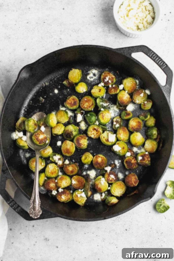 Roasted Brussels sprouts with goat cheese crumbles in a cast iron skillet, with a vintage spoon ready for serving.