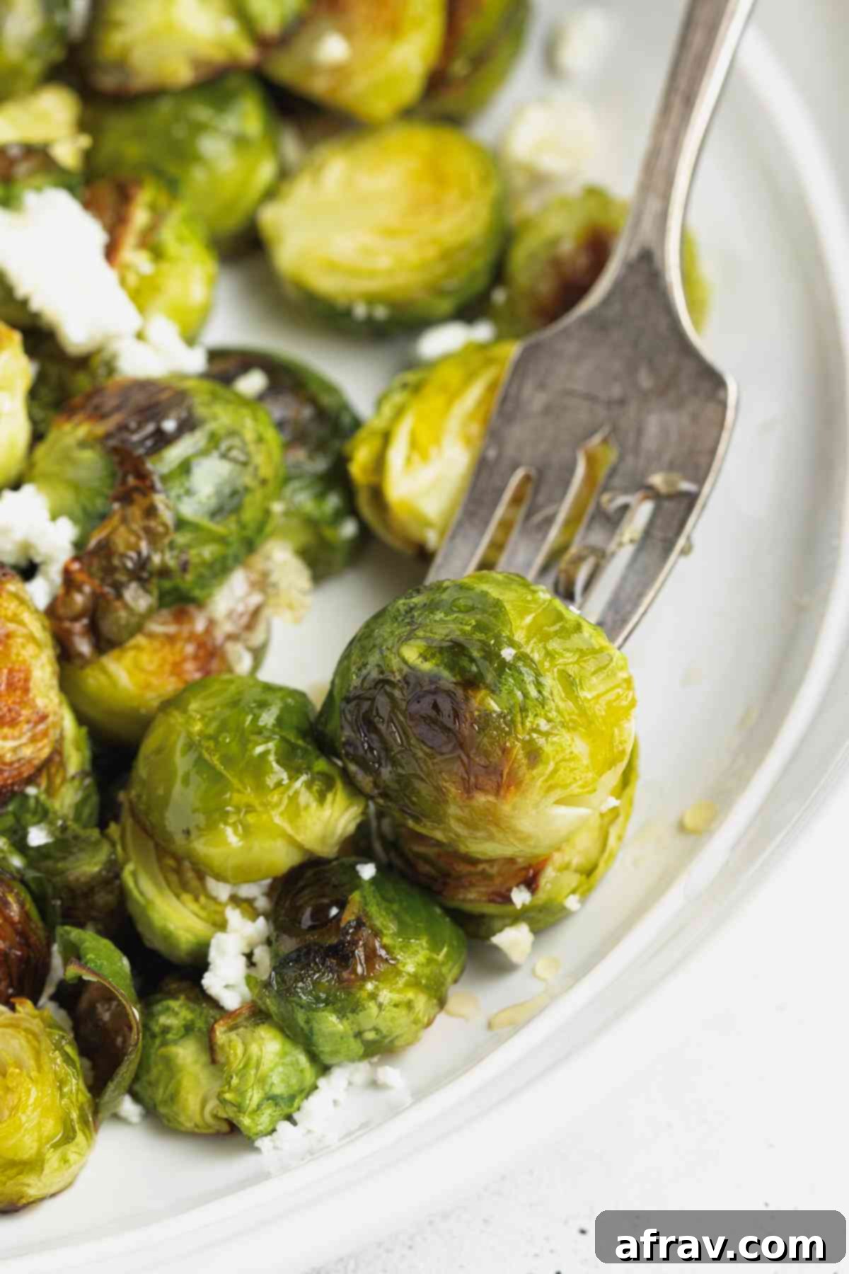 Vintage fork grabbing a crisped Brussels sprout from a round plate, inviting a taste.