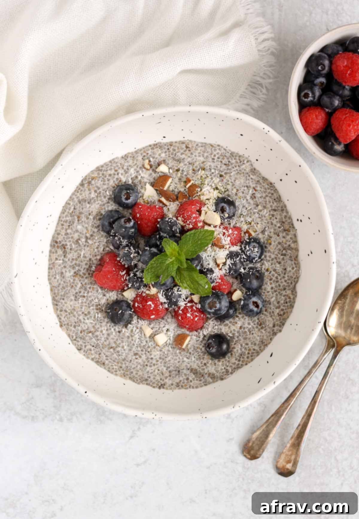 Chia seed breakfast bowl topped with fresh blueberries, raspberries, and chopped almonds with a side dish of berries.