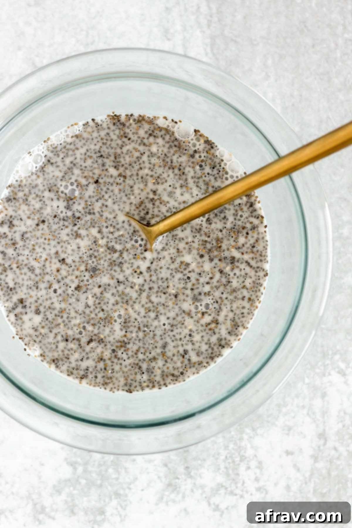 Chia seeds mixed with milk in a small glass mixing bowl.