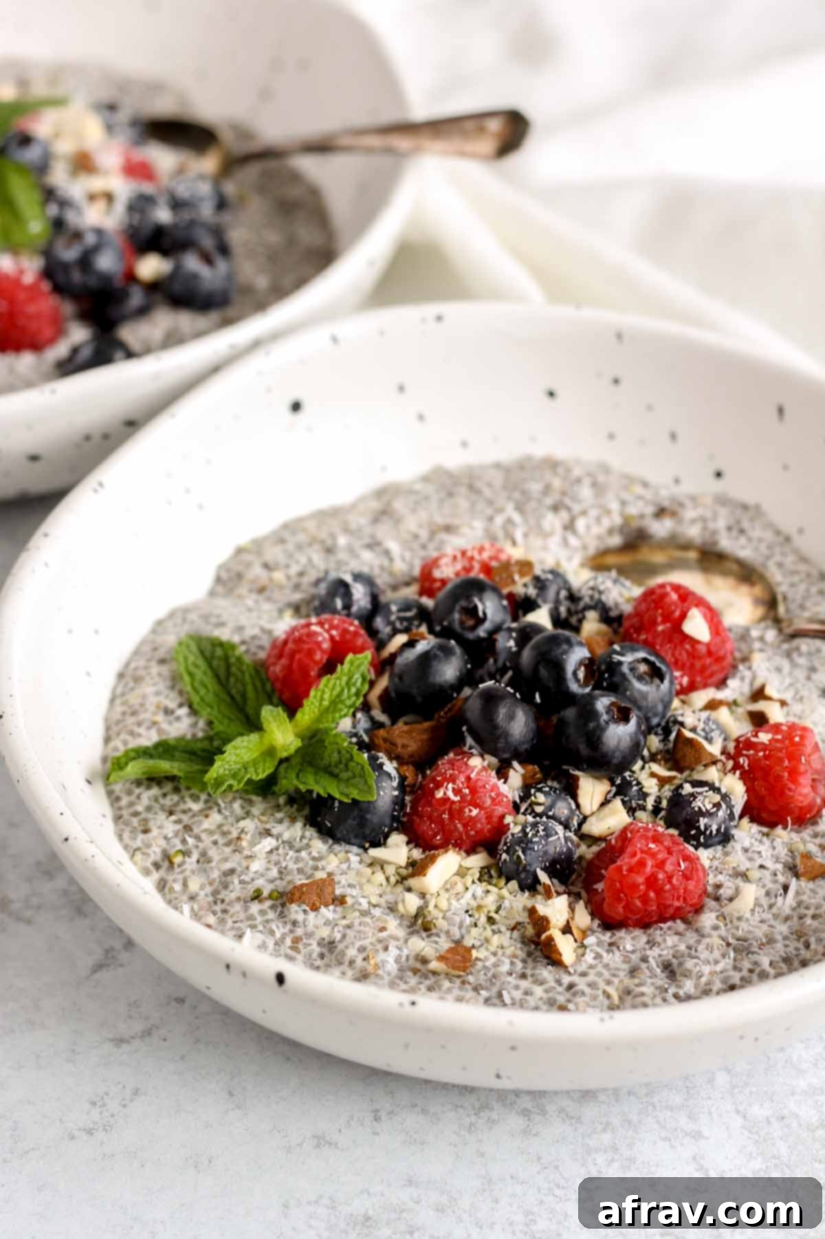 Chia pudding topped with blueberries, raspberries, and almonds in a shallow bowl with a vintage spoon in the bowl.