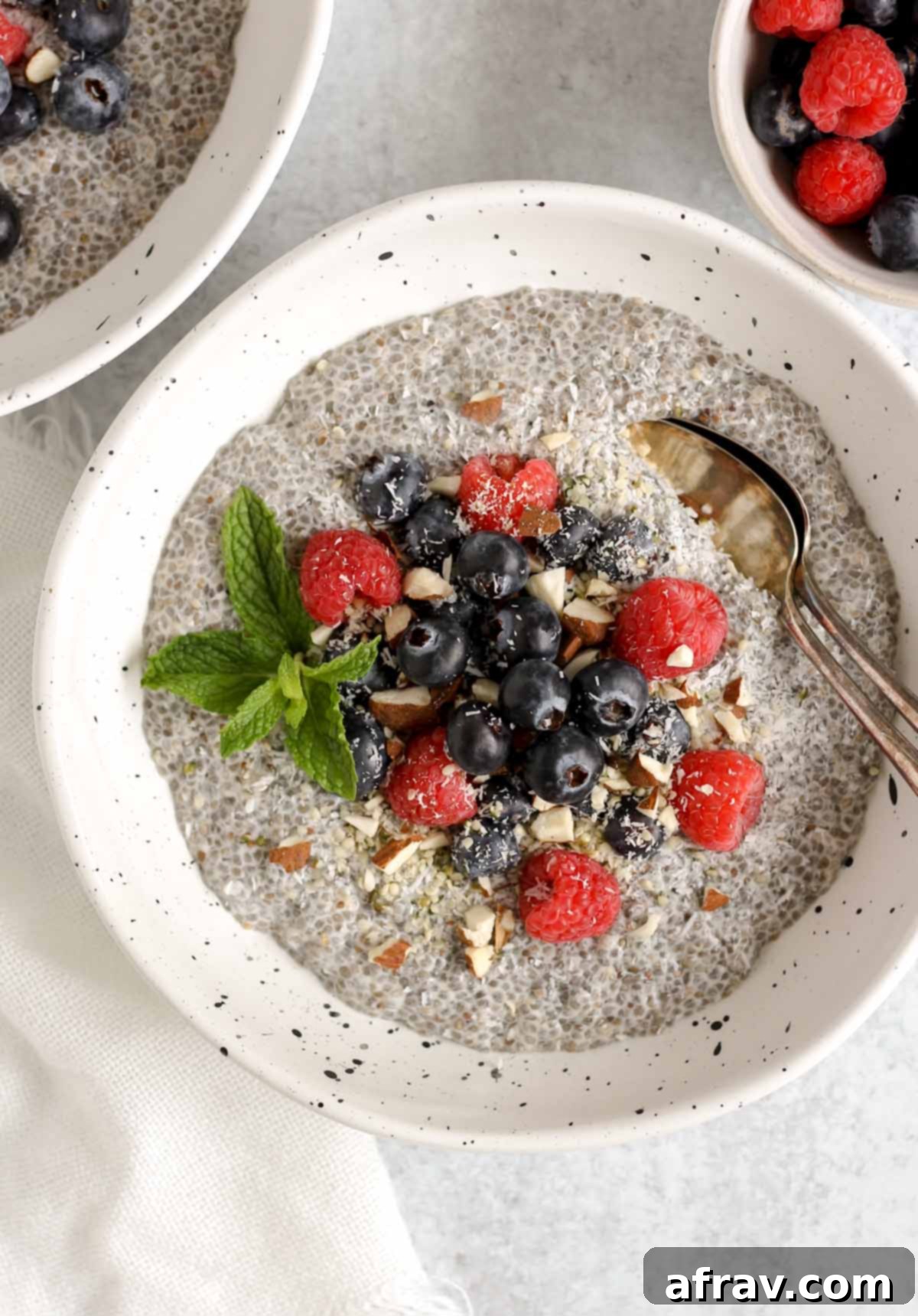 Chia seed breakfast bowl topped with fresh blueberries, raspberries, and chopped almonds with two vintage spoons in the bowl.