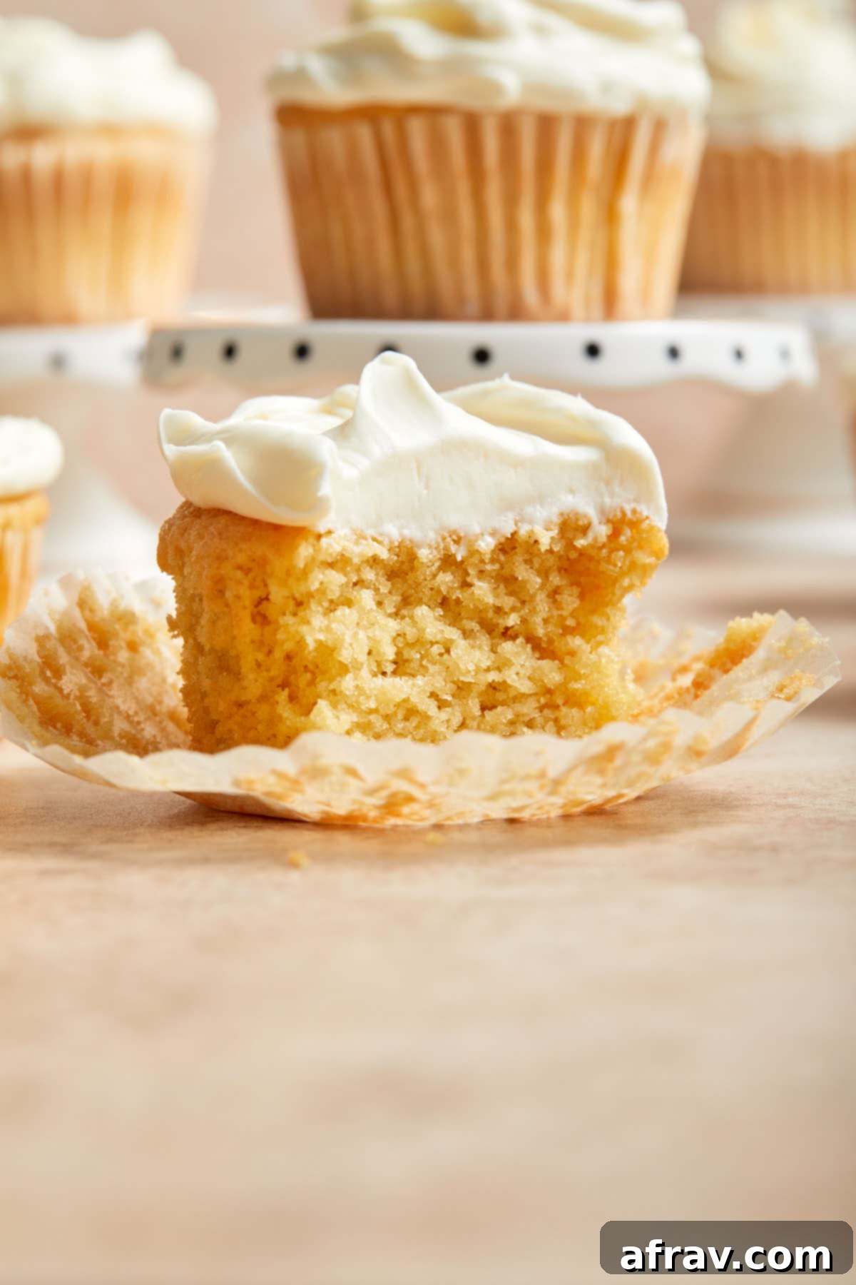 Side view of half a cupcake on a cupcake liner and exposing the inside texture. This perfectly showcases the tender and fluffy texture of the vanilla almond flour cupcake.