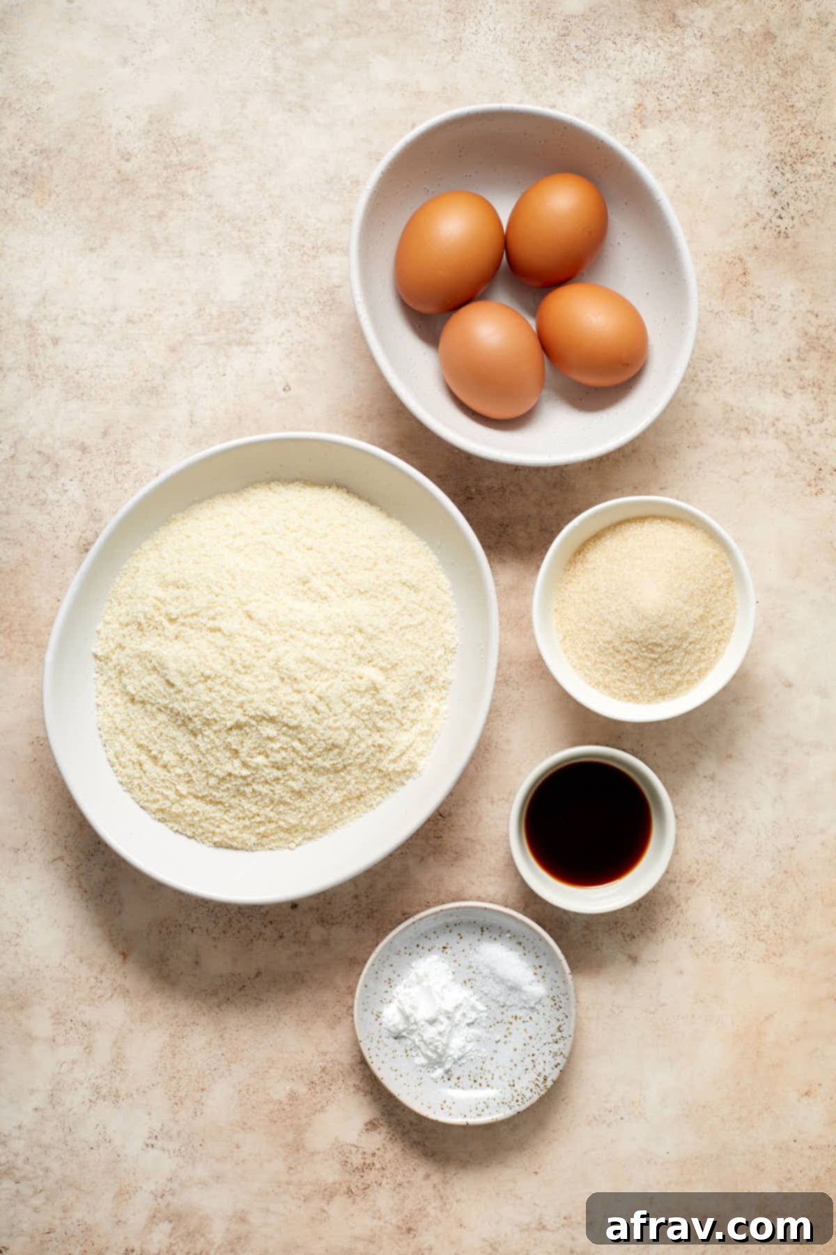 Ingredients to make almond flour cupcakes arranged in individual dishes. Featuring blanched almond flour, cane sugar, eggs, vanilla extract, baking powder, and salt.
