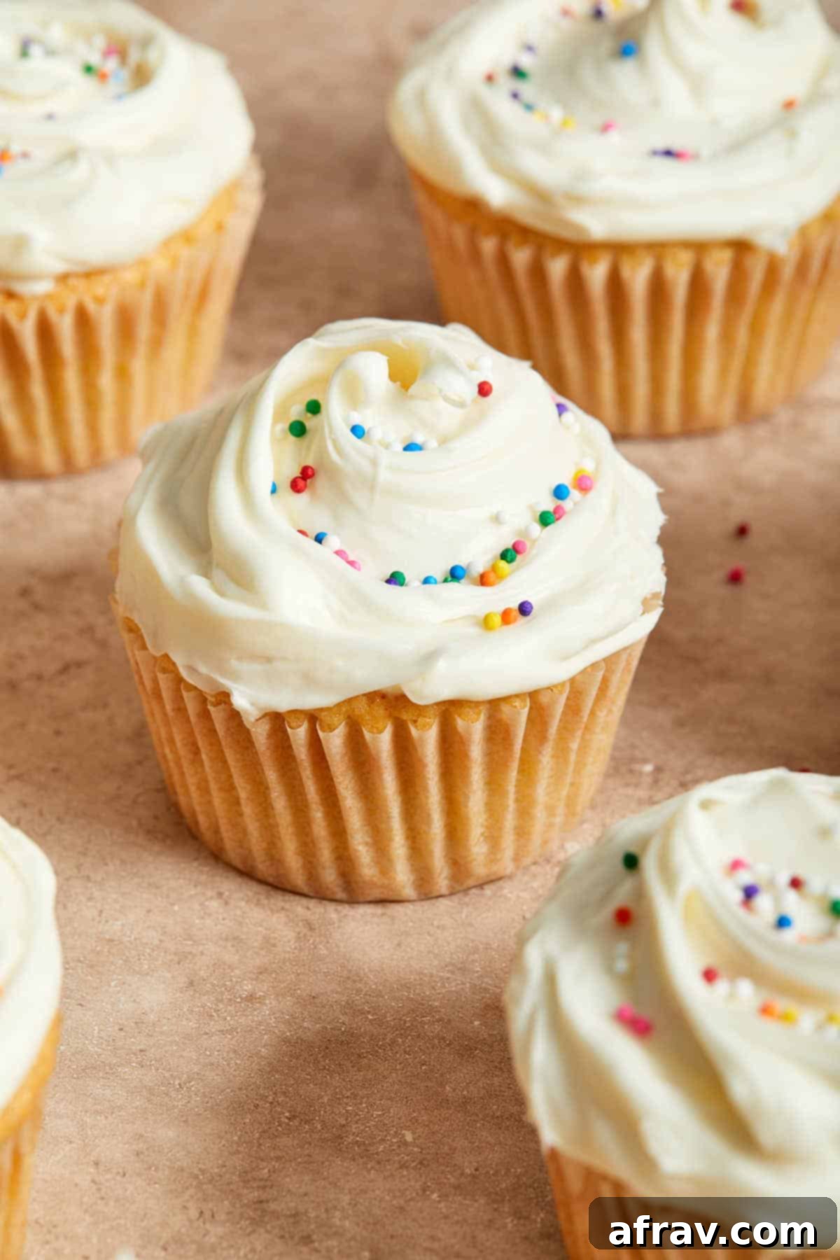 Frosted cupcakes with sprinkles, arranged on a beige coloured surface. These vanilla almond flour cupcakes are beautifully decorated.