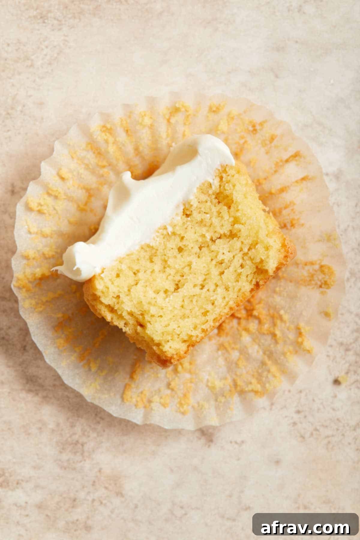 Overhead view of half a cupcake lying cut side up on a cupcake liner. The internal structure of the almond flour vanilla cupcake is visible.