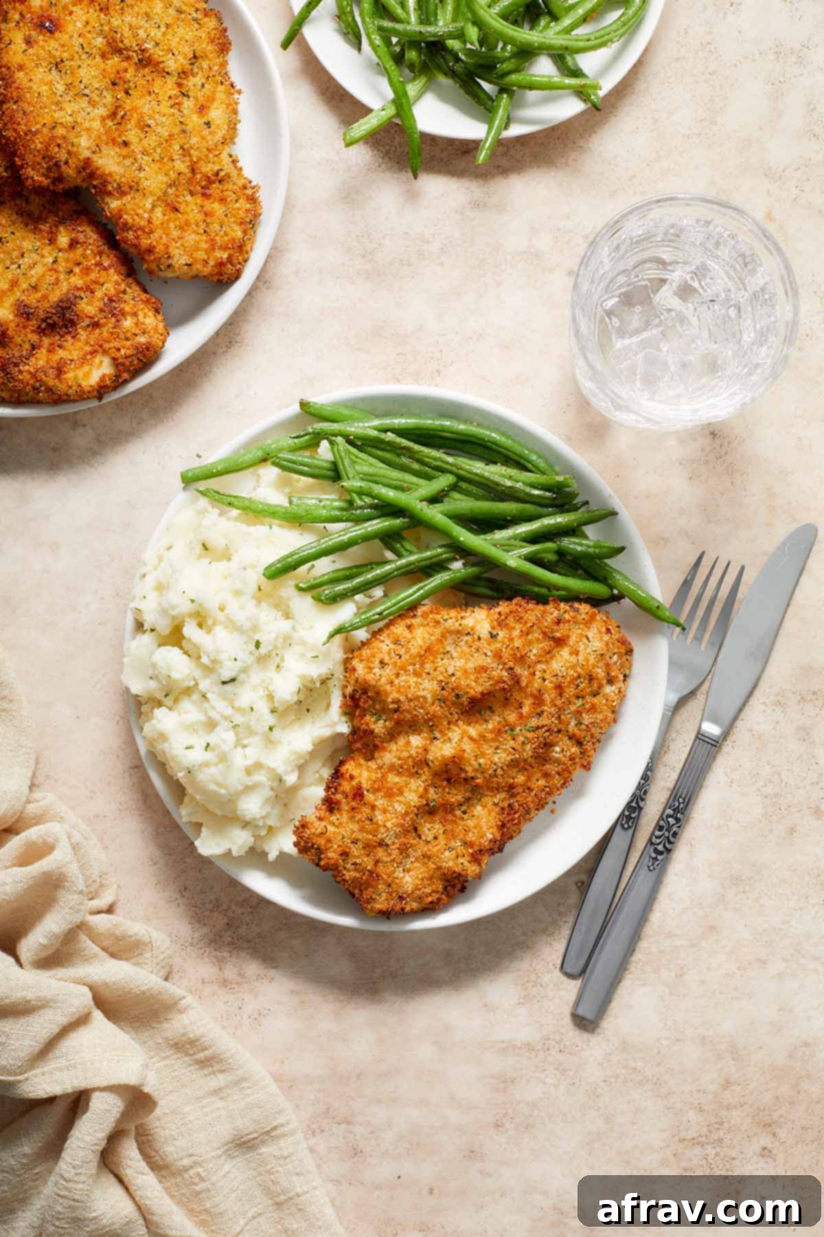 Overhead view of crispy Air Fryer Chicken Schnitzel, creamy mashed potatoes, and vibrant green beans on a plate, with additional plates in the background.