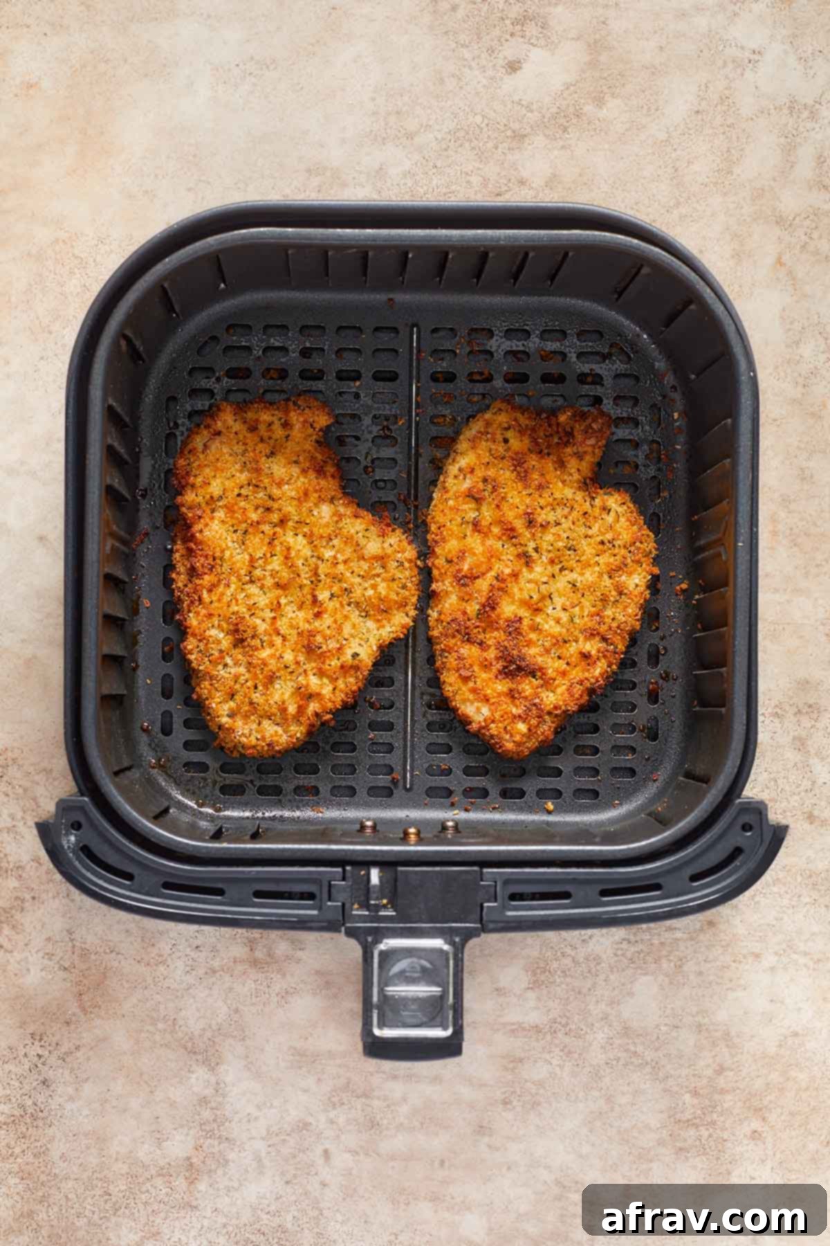 Freshly air fried chicken schnitzels, golden and crispy, cooling in an air fryer basket.