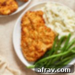 Air fryer chicken schnitzel on a white plate with mashed potatoes and green beans.