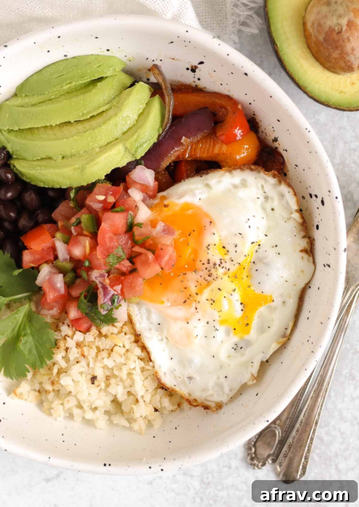 Breakfast burrito bowl topped with avocado and pico de gallo in a speckled bowl.
