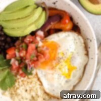 Breakfast burrito bowl topped with avocado and pico de gallo in a speckled bowl.