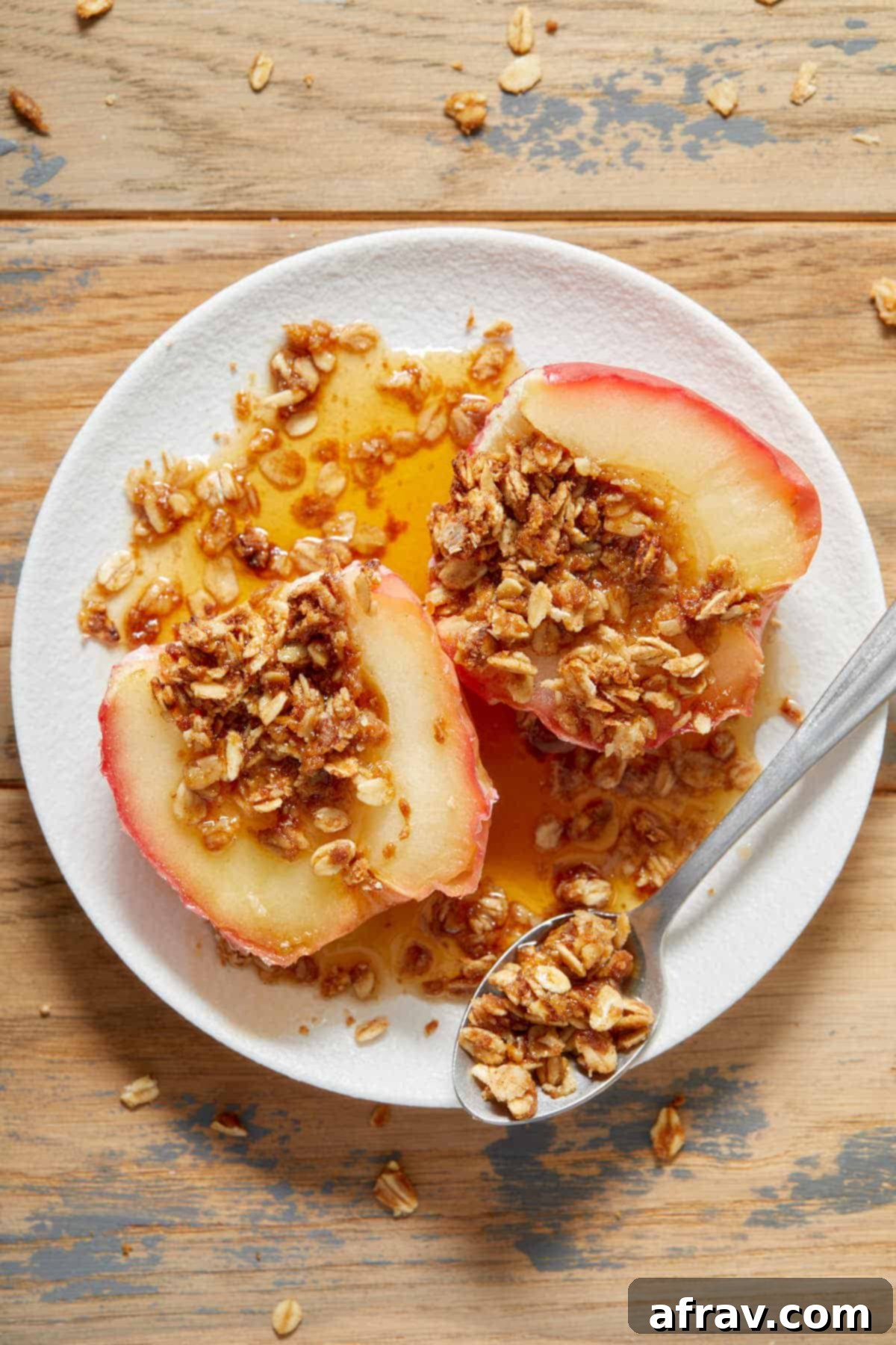 Overhead view of a stuffed air fryer baked apple on a white plate, cut in half with the cinnamon oat filling showing. A spoon rests beside it.
