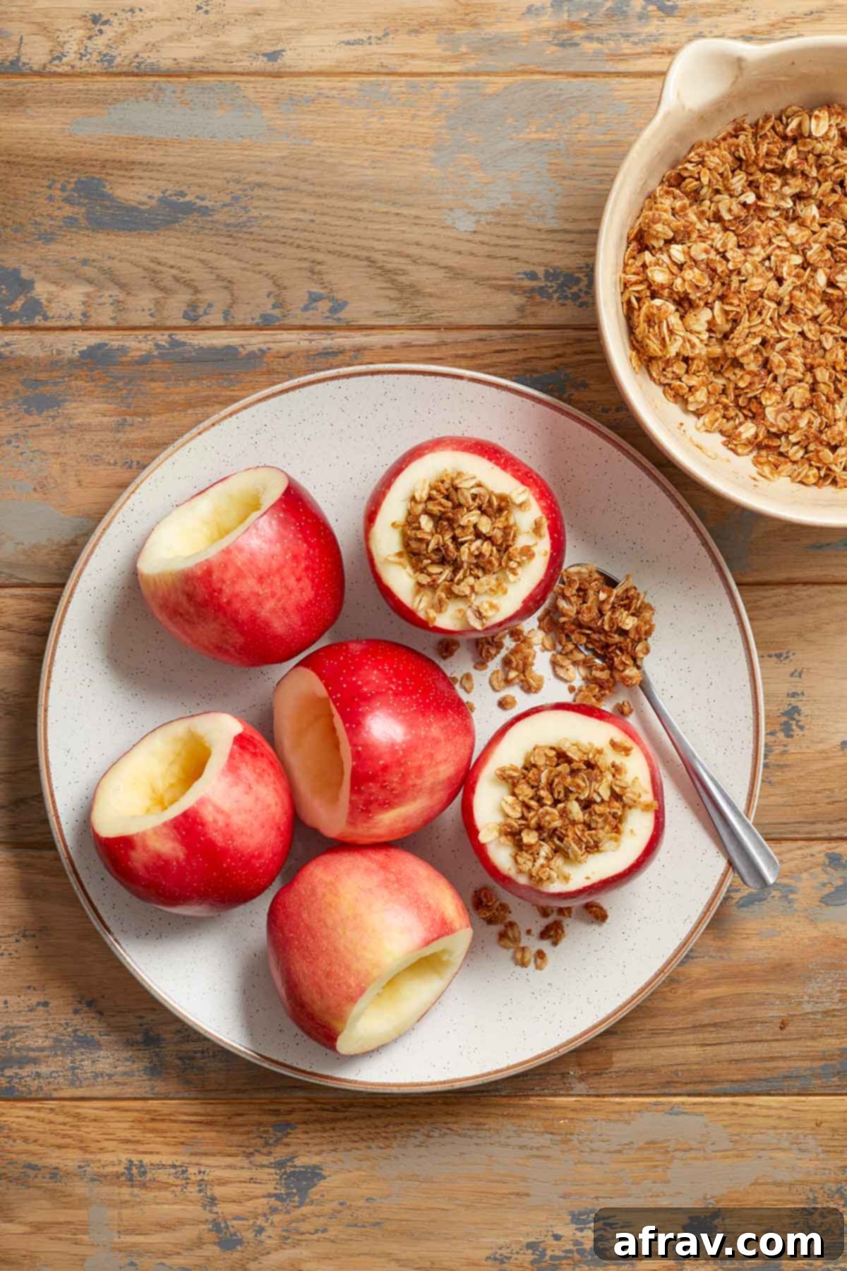 Cored apples on a white plate, with one apple being filled with the prepared oat mixture.