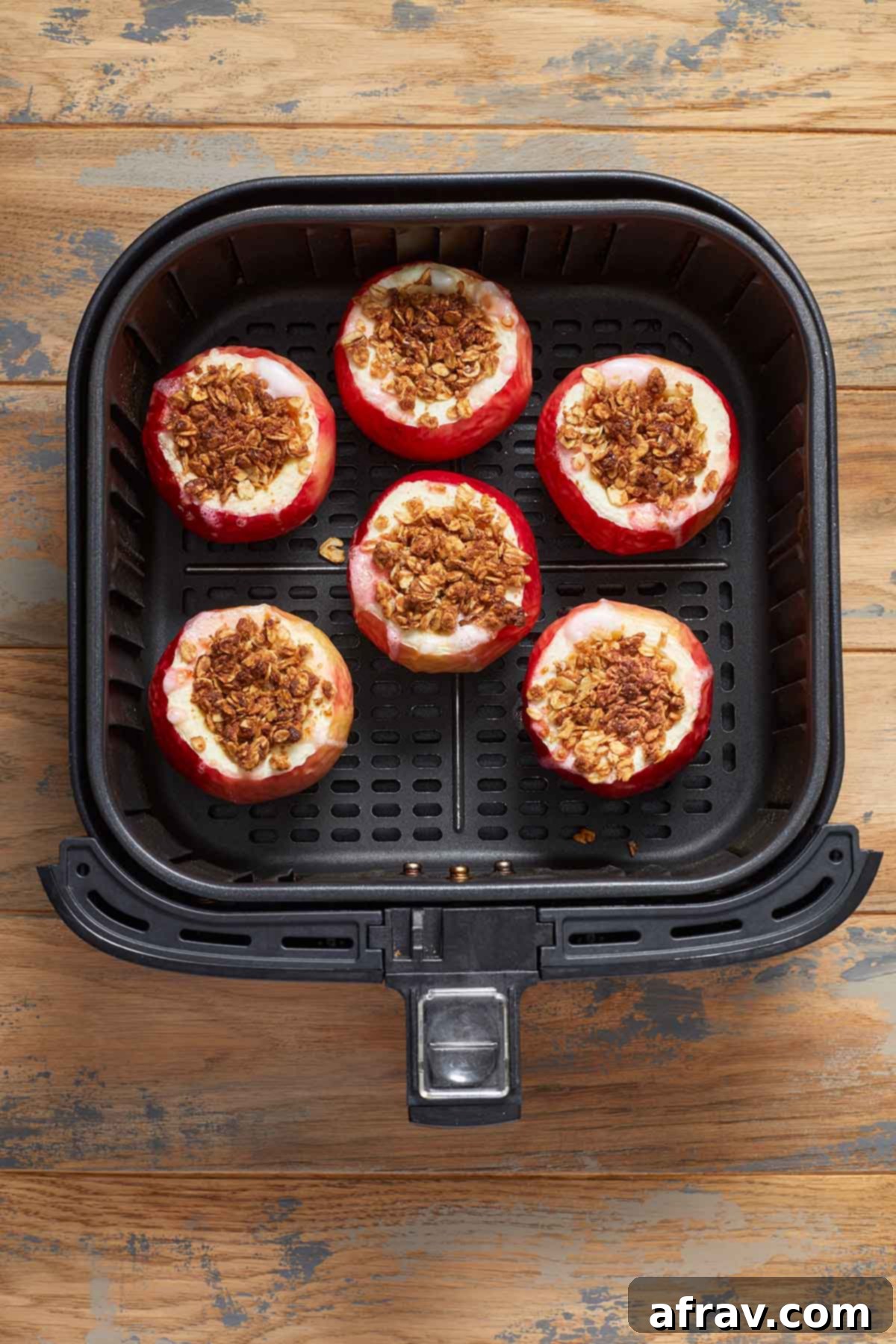 Perfectly baked apples, golden brown on top, resting inside the air fryer basket after cooking.