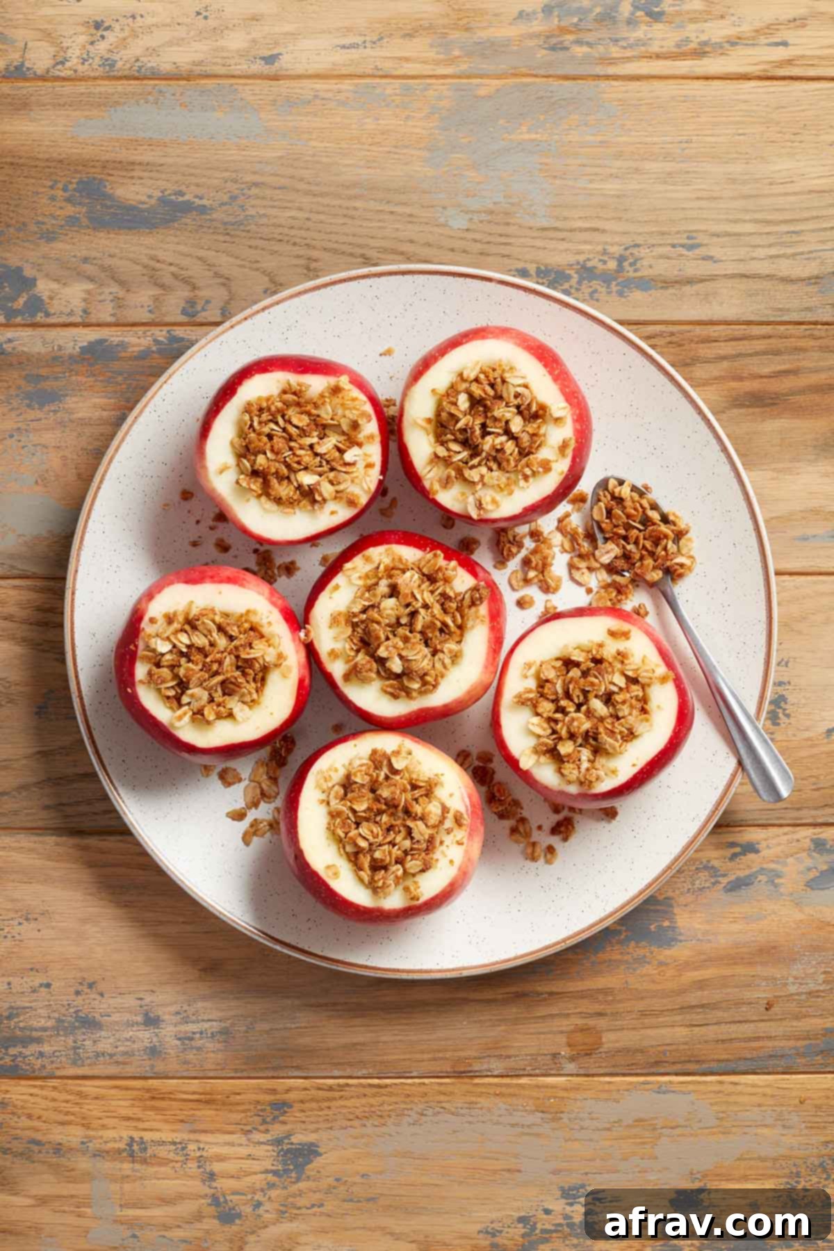 Six beautifully baked apples, golden brown and filled with cinnamon oat topping, arranged on a pristine white plate.