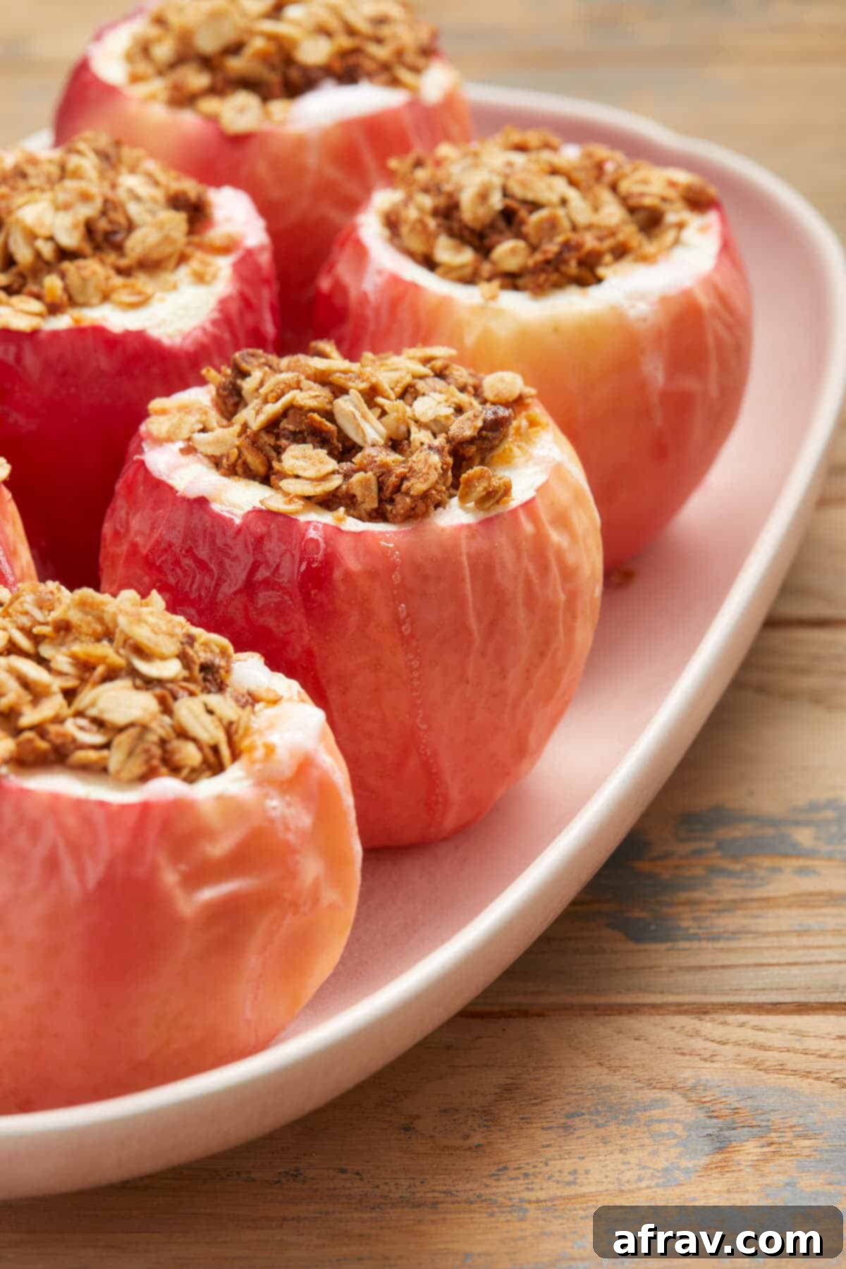 Side view of elegantly baked apples, each generously filled with cinnamon oat crumble, arranged on a vibrant pink platter.