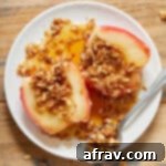 An air fryer baked apple, cut in half to show its delicious cinnamon oat filling, served on a white plate with a drizzle of maple syrup.