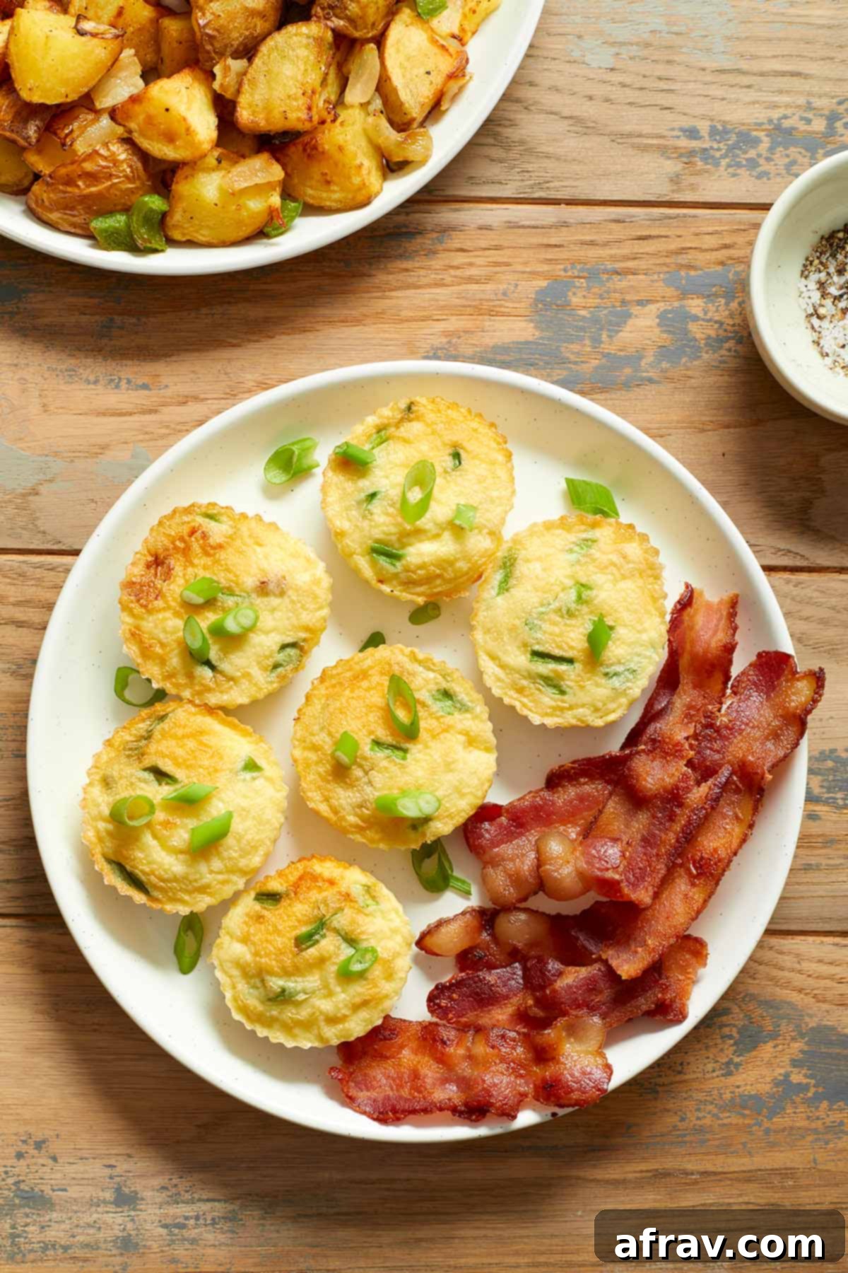 Egg muffins on a plate with slices of bacon and a plate of home fries on the side.