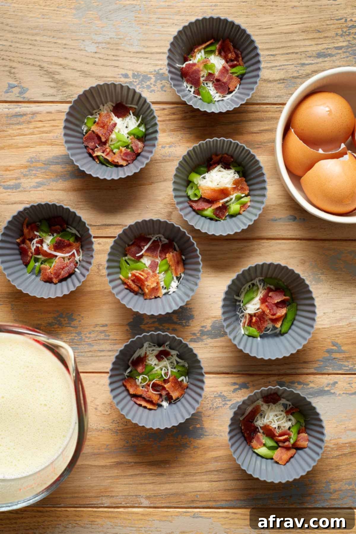 Silicone muffin cups filled with bacon, cheese and green onion with the egg mixture in a cup on the side.