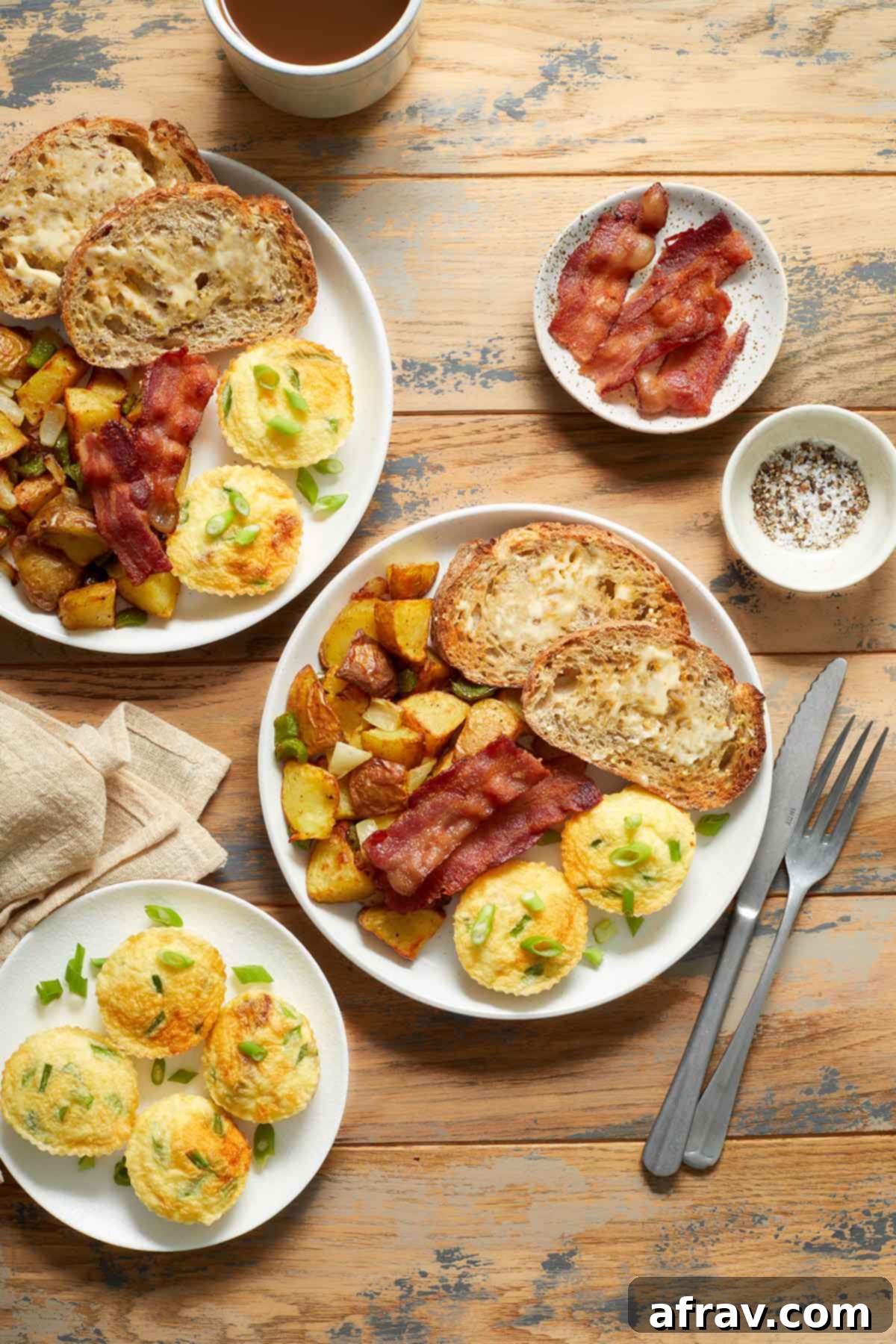 A breakfast setting with plates of egg bites, bacon, home fries and toast on a wooden table.
