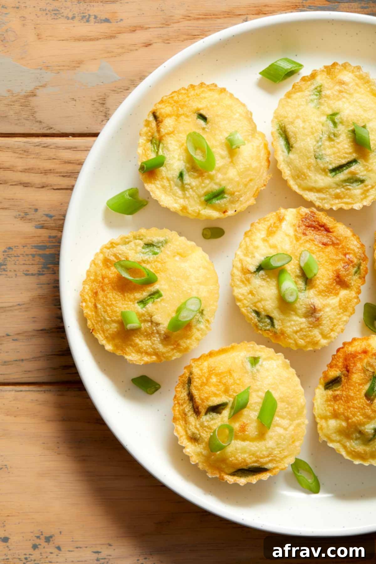 Close up view of egg bites on a white plate and topped with chopped green onions.