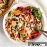 Asian cabbage salad sprinkled with sesame seeds and fresh cilantro in a small white bowl with two vintage forks.