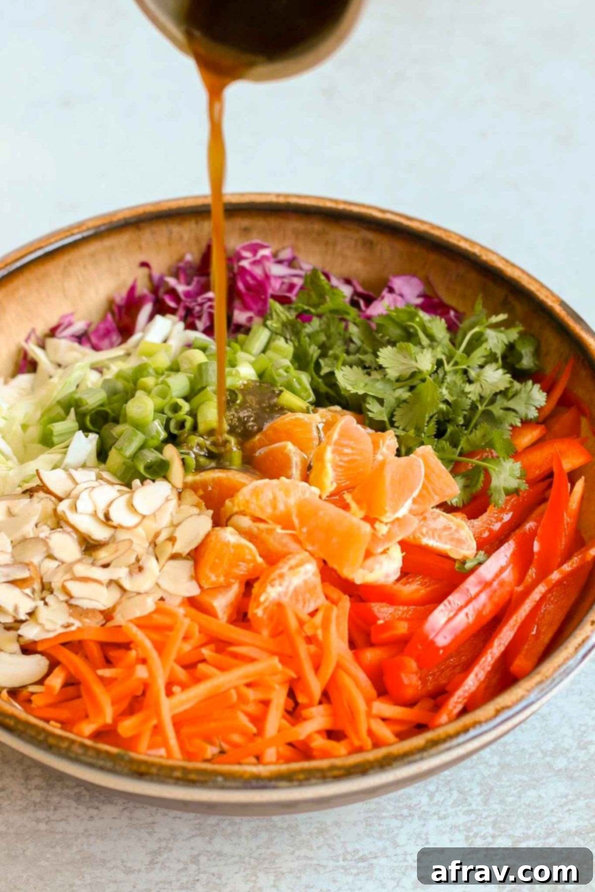 Dressing being poured on top of Asian cabbage salad ingredients in a large ceramic bowl.