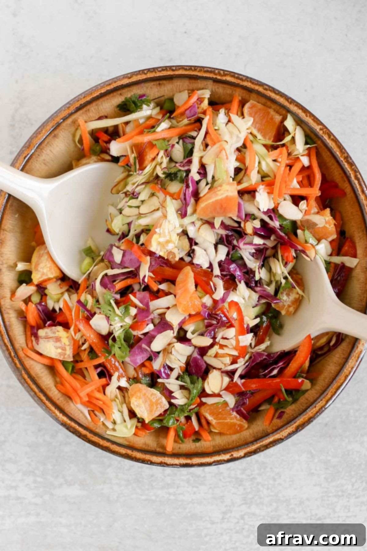 Asian cabbage salad being mixed with dressing in a large ceramic bowl.