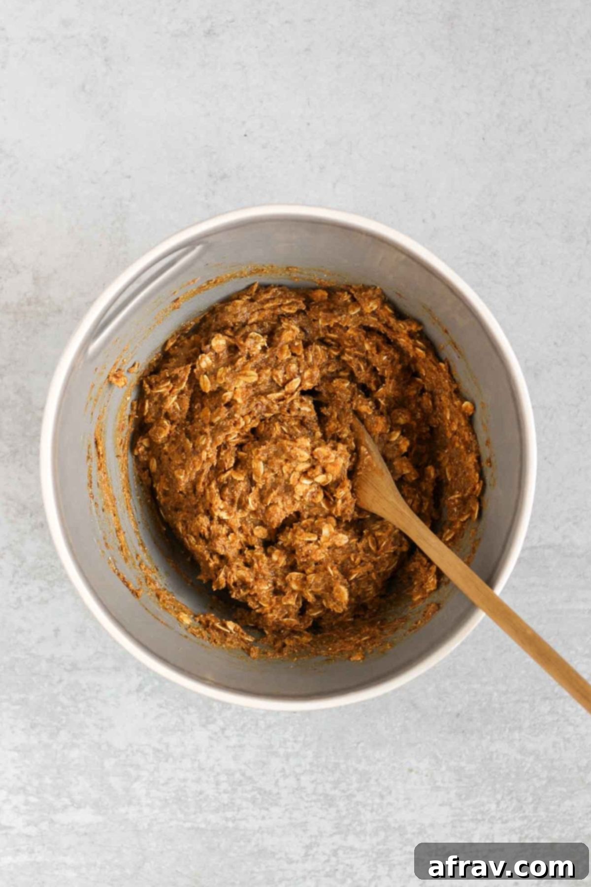 Grab-and-Go Pumpkin Breakfast Cookies 5 Pumpkin breakfast cookie dough in a mixing bowl, being mixed with a wooden spoon.
