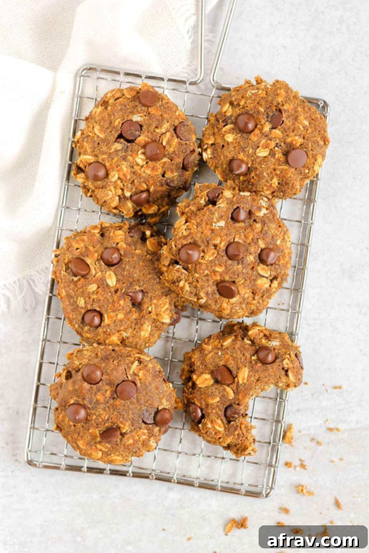 Grab-and-Go Pumpkin Breakfast Cookies 10 A selection of pumpkin breakfast cookies, with one bite taken out, resting on a rectangular wire cooling rack.