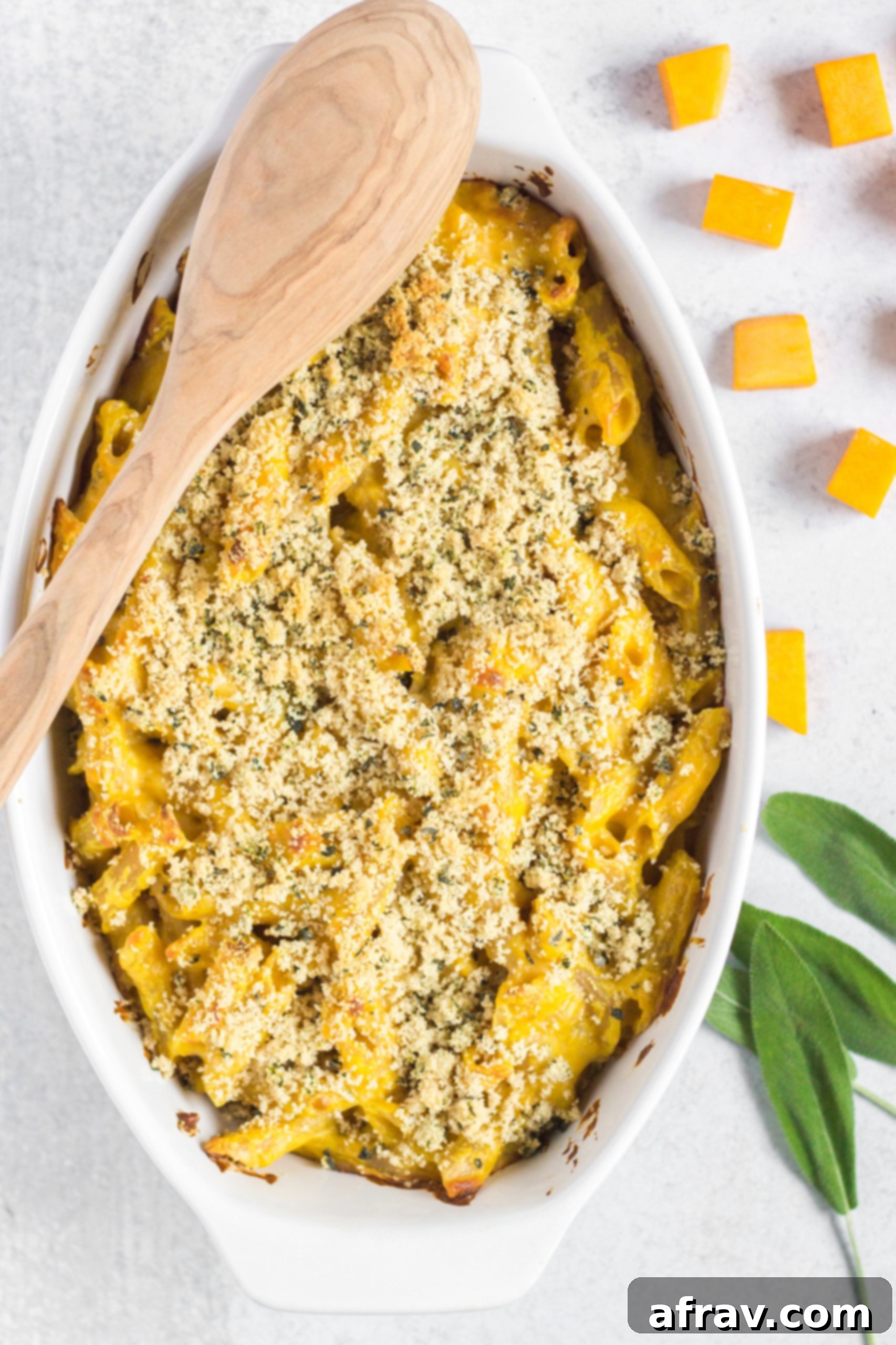 A serving dish of creamy gluten-free baked butternut squash mac and cheese, ready to be enjoyed, with a wooden spoon.