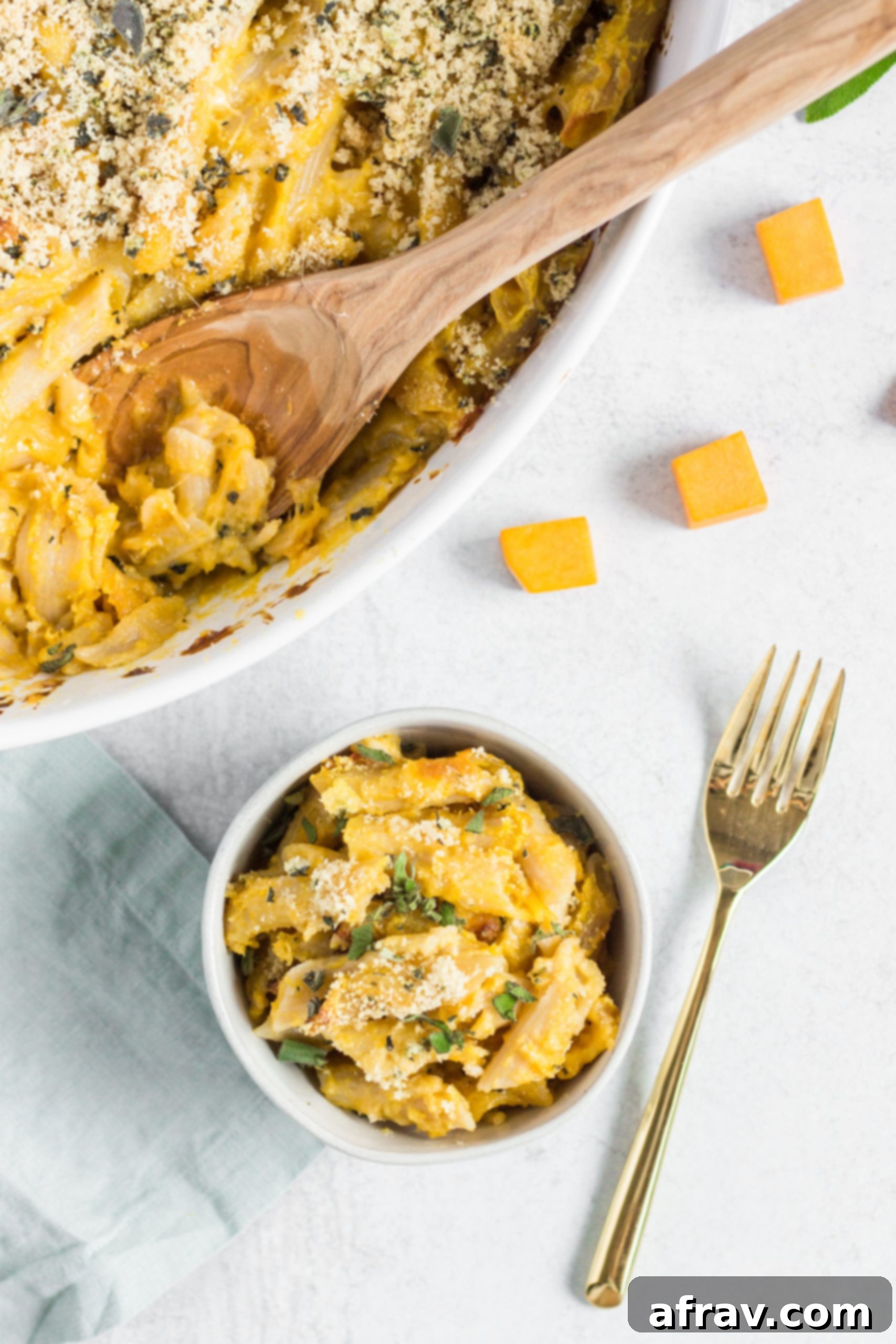 A small white bowl filled with individual serving of gluten-free butternut squash mac and cheese, garnished with fresh herbs.