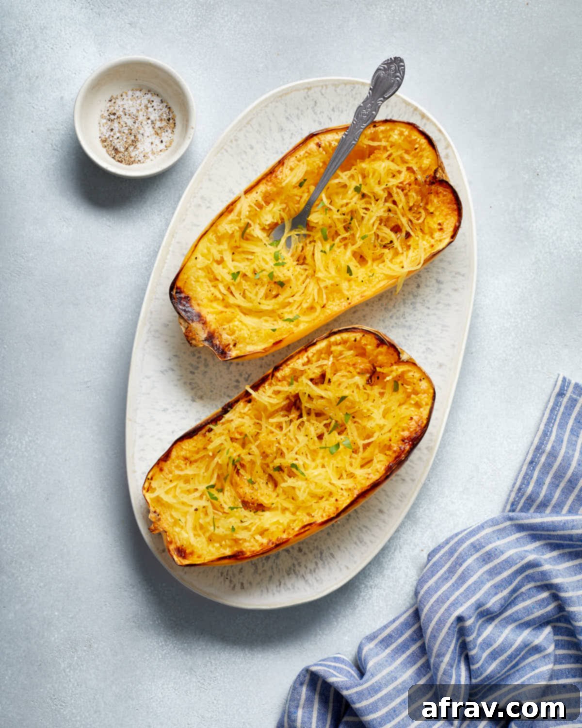 Two halves of golden brown air-fried spaghetti squash, seasoned and ready to be forked, arranged on a platter with a blue napkin on the side.