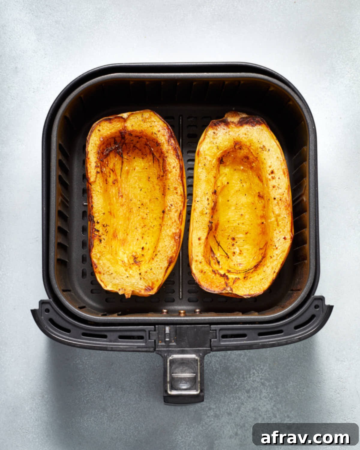 The two roasted spaghetti squash halves, golden brown and perfectly cooked, resting inside the air fryer basket after frying.