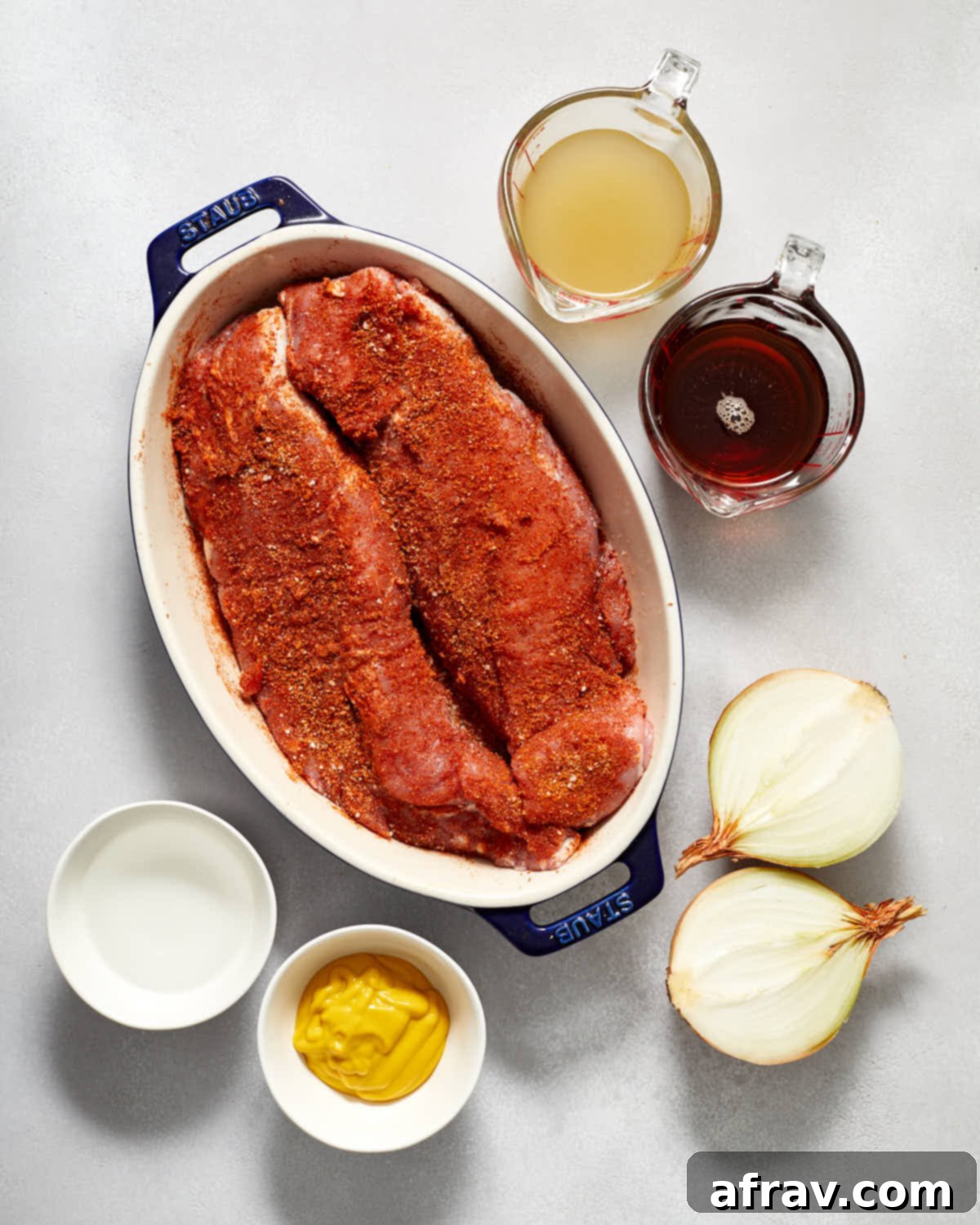 Pork tenderloins coated in spice mixture, ready for the slow cooker, with other ingredients surrounding it.