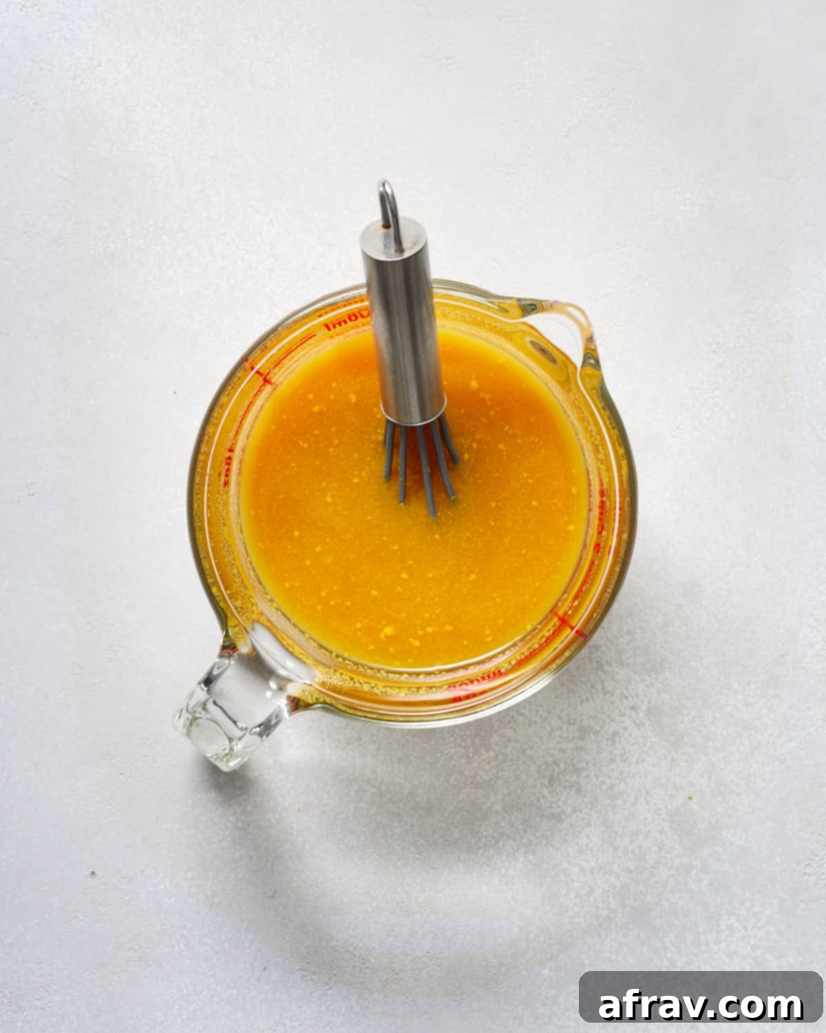 Maple syrup and mustard mixture being whisked together in a glass measuring cup.